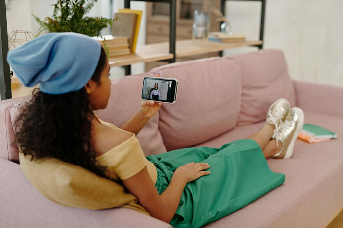 Woman relaxing on a couch, watching a video on her phone, possibly about mom-relationship-drama. Woman relaxing on a couch, watching a video on her phone, possibly about mom-relationship-drama.