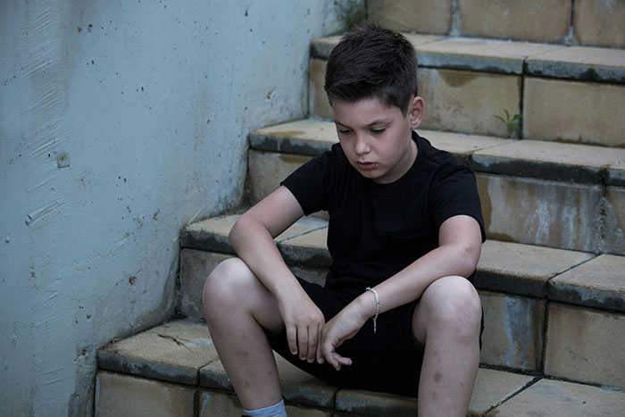 A young boy in a pensive mood sitting on stairs, challenging the born gifted stereotype.
