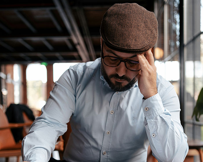 Man in glasses and a cap, deep in thought, sitting in a cozy cafe.