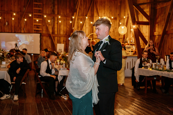 Groom dancing with mother at a summer wedding reception in a wooden barn venue, surrounded by guests. Groom dancing with mother at a summer wedding reception in a wooden barn venue, surrounded by guests.