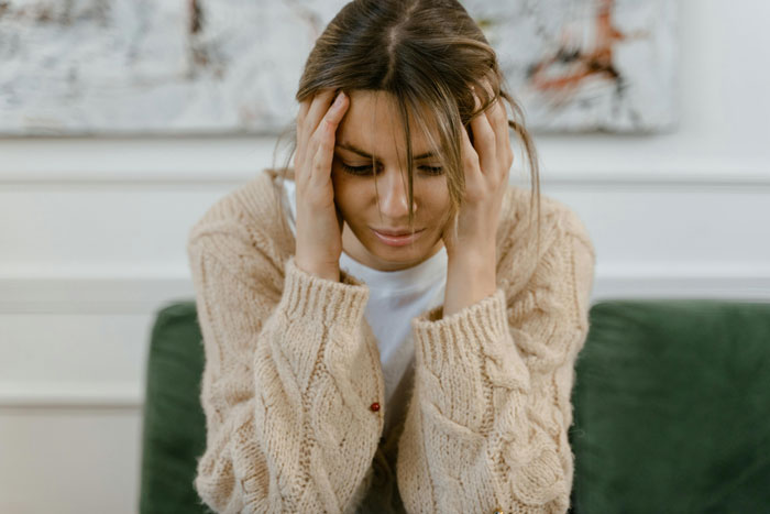 Woman in beige sweater sitting on a green couch, appearing distressed about a neighbour-daughter-husband-affair. Woman in beige sweater sitting on a green couch, appearing distressed about a neighbour-daughter-husband-affair.