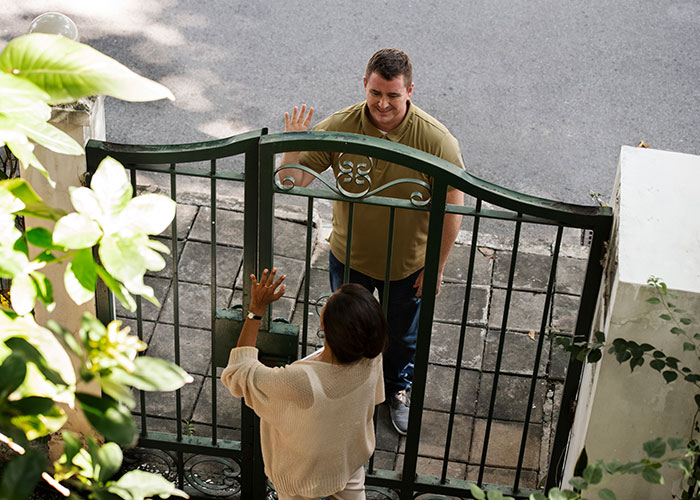 Couple in town greeting neighbor through gate, expecting a warm welcome. Couple in town greeting neighbor through gate, expecting a warm welcome.