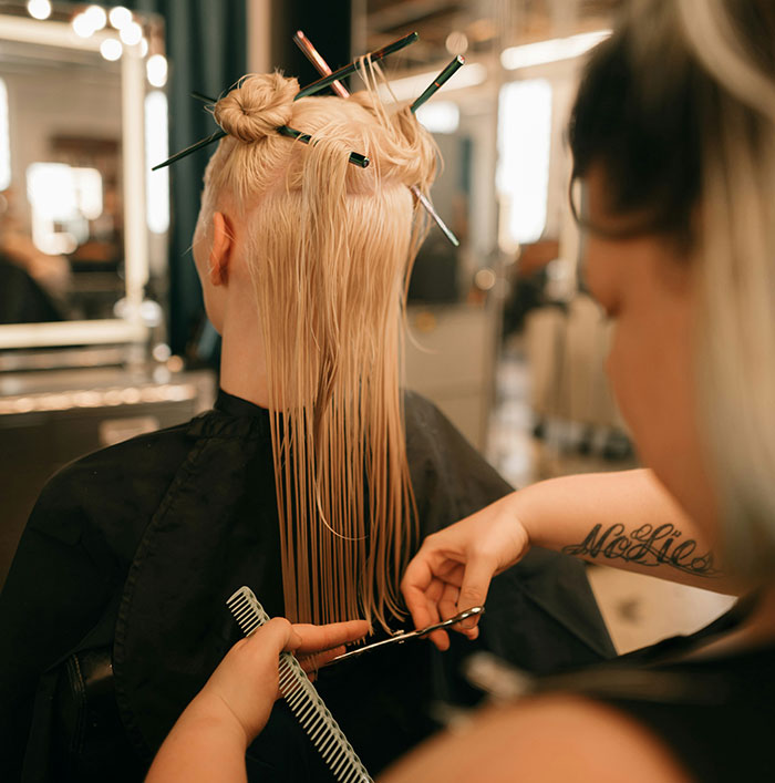A woman getting a haircut in a salon, showing transformation and self-awareness with a stylist cutting her blonde hair. A woman getting a haircut in a salon, showing transformation and self-awareness with a stylist cutting her blonde hair.