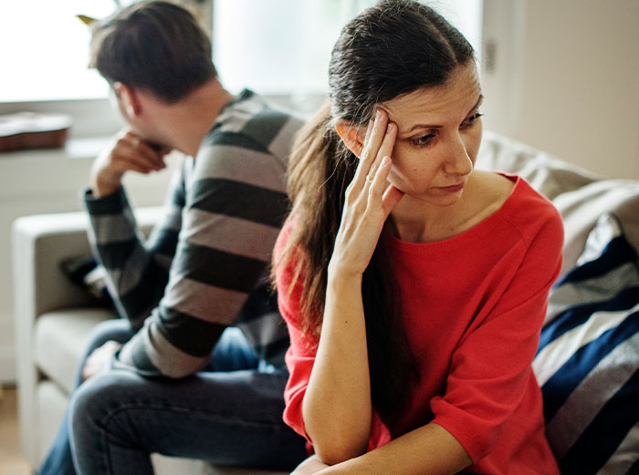 Upset couple sitting on a couch, woman in red shirt looking troubled, highlighting conflict over daughter's junk food diet. Upset couple sitting on a couch, woman in red shirt looking troubled, highlighting conflict over daughter's junk food diet.