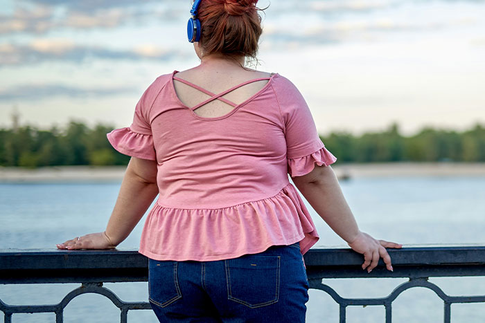 A girl wearing headphones and a pink top, standing by a riverside railing. A girl wearing headphones and a pink top, standing by a riverside railing.