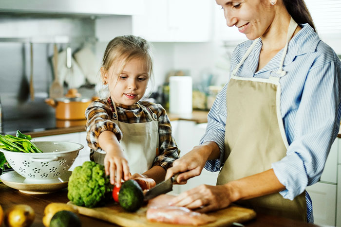 Mother and daughter cooking healthy food together in a kitchen, wearing aprons and smiling. Mother and daughter cooking healthy food together in a kitchen, wearing aprons and smiling.