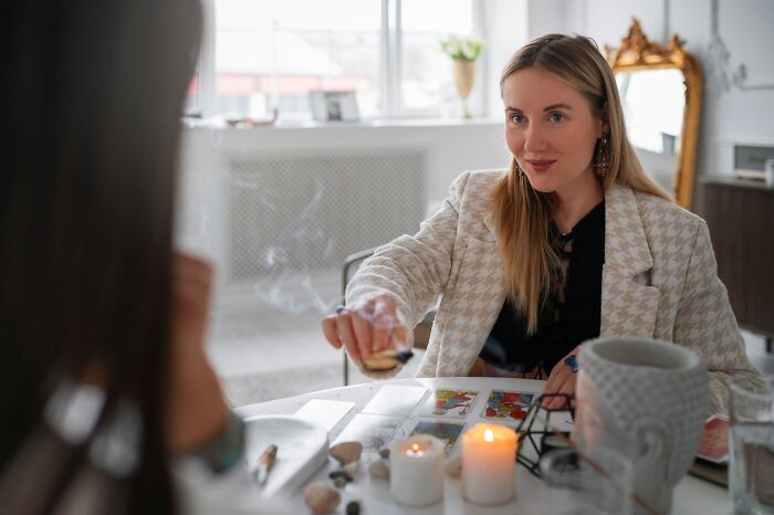 A woman in a stylish blazer performs a tarot reading with candles, representing an occupation from heroic to hilarious over the years.