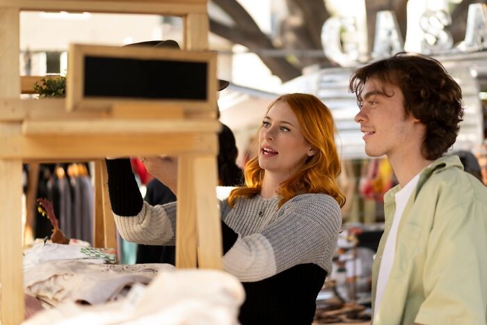 Two people browsing items at an outdoor market stall, engaging in conversation.