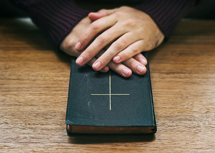 Hands resting on a closed book with a cross on the cover, symbolizing persistent Mormons' faith and learning. Hands resting on a closed book with a cross on the cover, symbolizing persistent Mormons' faith and learning.