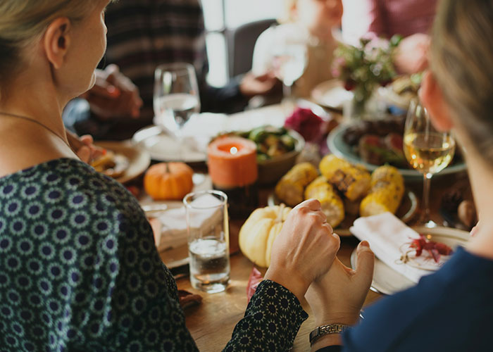 People gathered around a dinner table, holding hands in a moment of gratitude, with a variety of food and candles. People gathered around a dinner table, holding hands in a moment of gratitude, with a variety of food and candles.