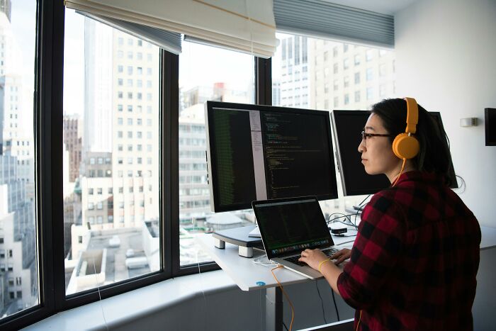 Person coding at a standing desk with multiple monitors.