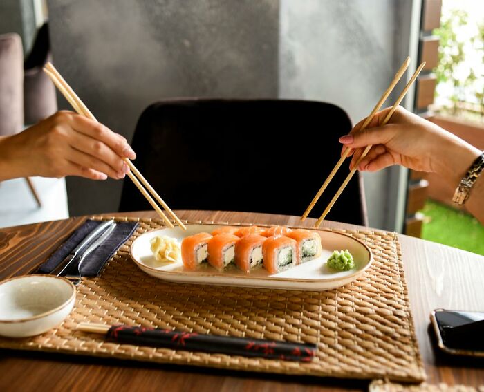 Two people using chopsticks to share sushi, symbolizing kindness and generosity.
