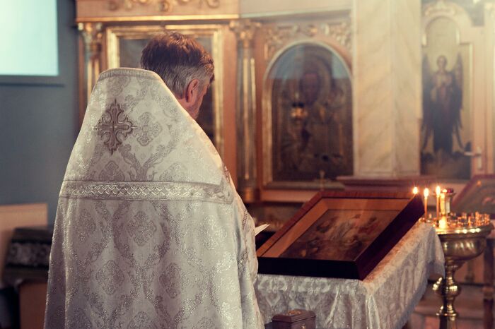 Priest in ornate robe at altar, illustrating shift in occupations from heroic to humorous over time.