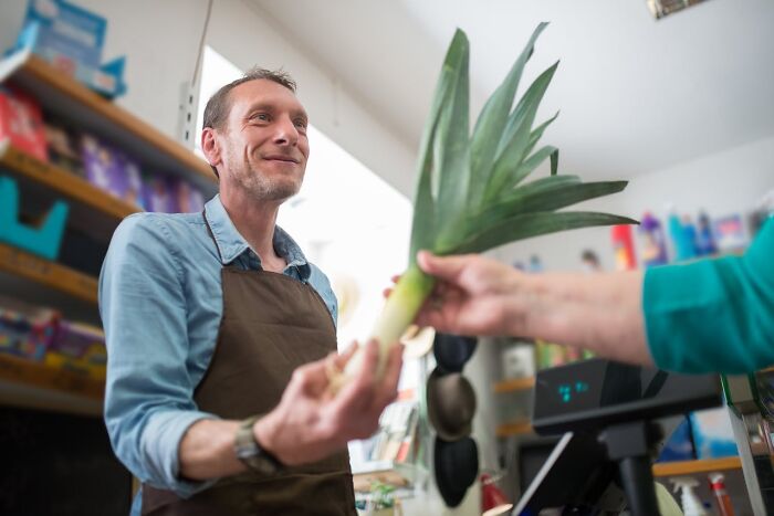 Person in a store, smiling while handing a leek to a customer, illustrating traits of a good person.