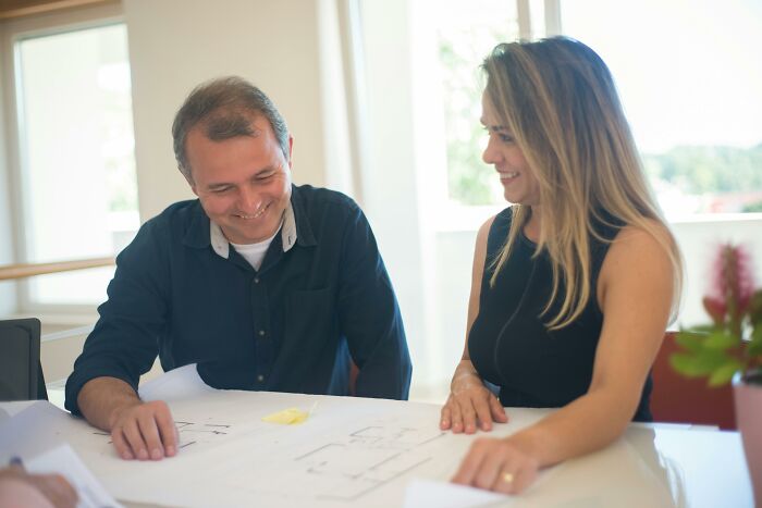 Two people at a table reviewing plans, illustrating the shift of heroic occupations to more humorous ones over time.