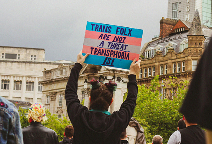 Protester holding a sign about trans rights amidst city buildings, reacting to JK Rowling's comments. Protester holding a sign about trans rights amidst city buildings, reacting to JK Rowling's comments.