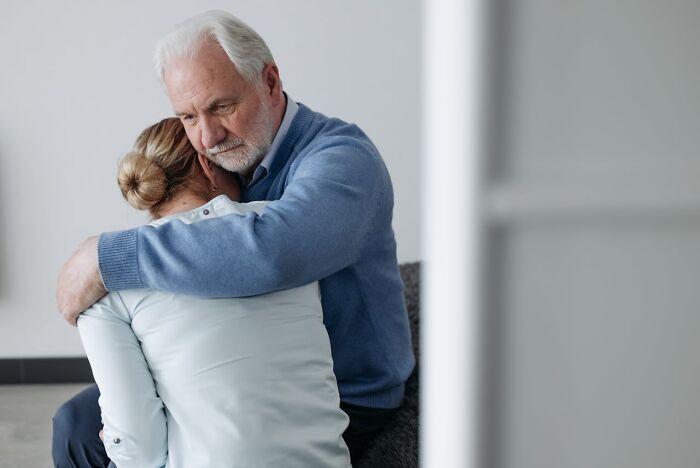 Elderly man in a blue sweater comforting a person, showing a small act of kindness.