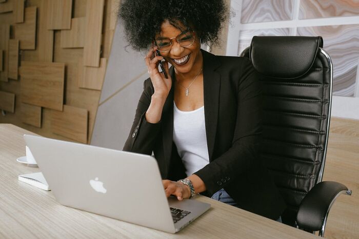 Smiling woman on phone, working on a laptop, representing traits of a truly good person.