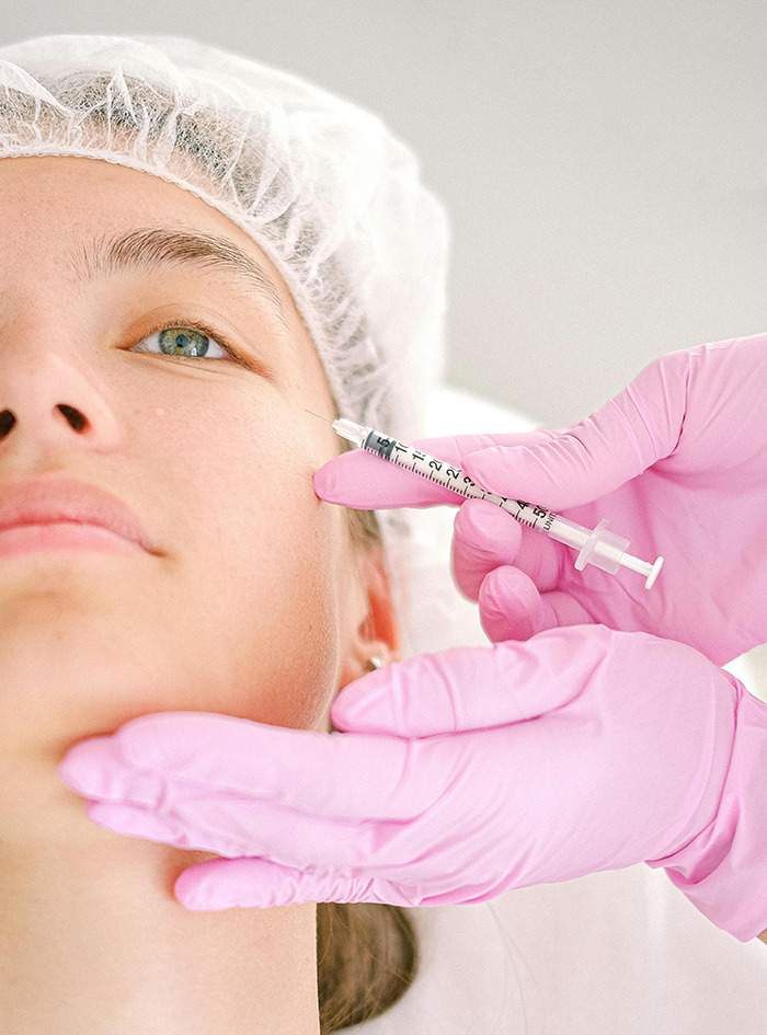Person receiving Botox injection, healthcare professional wearing pink gloves and a hair cap. Person receiving Botox injection, healthcare professional wearing pink gloves and a hair cap.