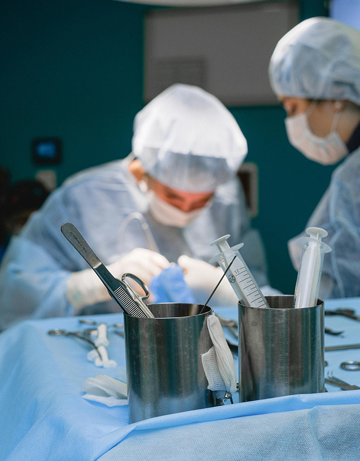 Surgeons performing surgery with instruments and syringes in focus on a sterile table. Surgeons performing surgery with instruments and syringes in focus on a sterile table.