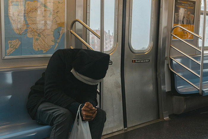 Person in a hoodie sitting on a subway, face hidden, holding a bag. Person in a hoodie sitting on a subway, face hidden, holding a bag.