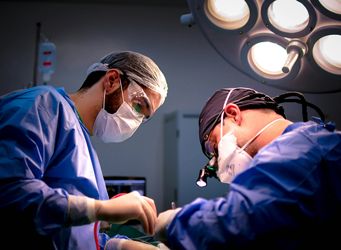 Surgeons in operating room, wearing masks and scrubs under bright surgical lights. Surgeons in operating room, wearing masks and scrubs under bright surgical lights.