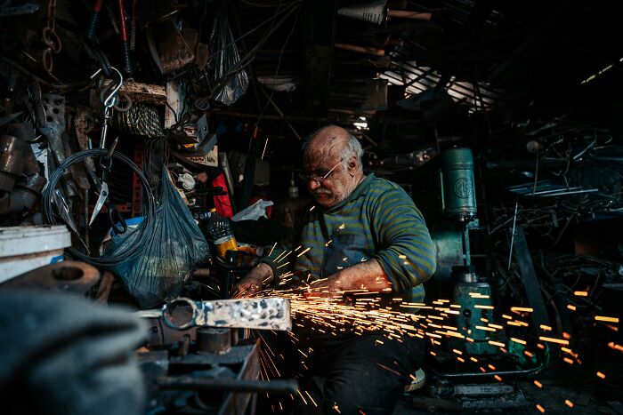 An older man working as a welder in a cluttered workshop, highlighting the evolution of occupations.