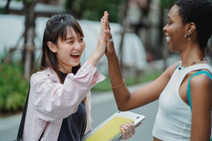 Two friends smiling and high-fiving, showcasing good person traits in a friendly street setting.
