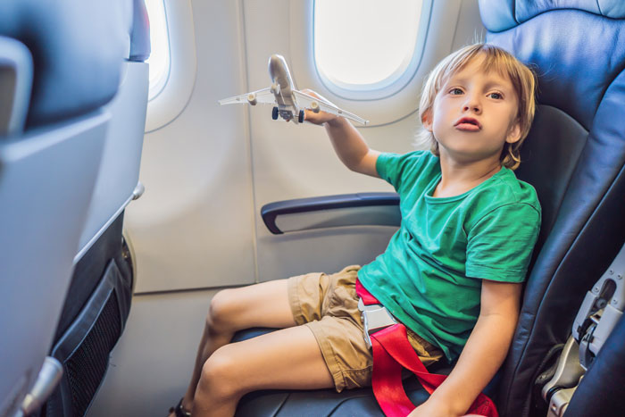Child with toy plane in airplane seat, green shirt, looking out window. Child with toy plane in airplane seat, green shirt, looking out window.