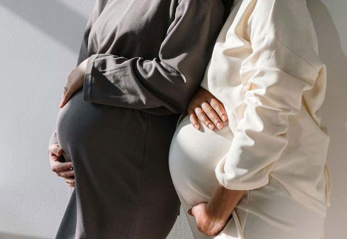 Two pregnant friends standing side by side, wearing comfortable clothing and gently touching their bellies. Two pregnant friends standing side by side, wearing comfortable clothing and gently touching their bellies.