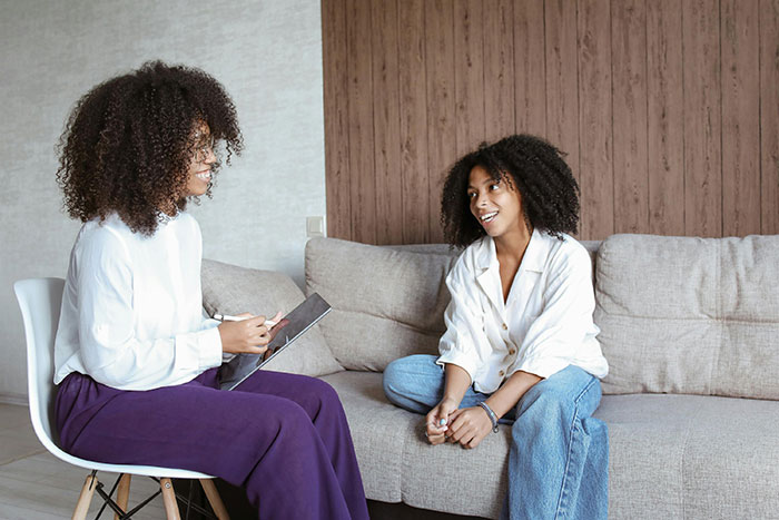 Two women having a discussion on a sofa, one writing notes. Two women having a discussion on a sofa, one writing notes.