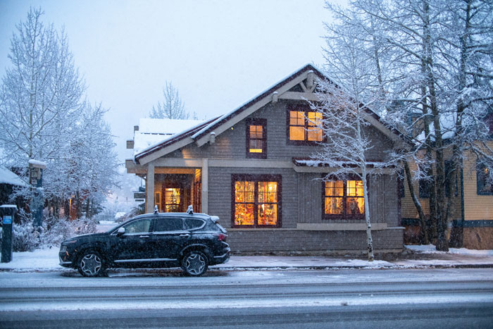 Snow-covered house with warm interior lights, trees, and parked car, reflecting winter scene in a neighborhood. Snow-covered house with warm interior lights, trees, and parked car, reflecting winter scene in a neighborhood.