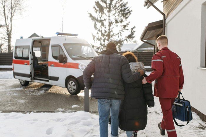 Paramedic assists two people walking through snow towards an ambulance. Paramedic assists two people walking through snow towards an ambulance.