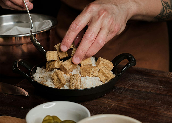Person preparing food with rice and cubes in a black dish, illustrating the refusal to deliver baby shower food. Person preparing food with rice and cubes in a black dish, illustrating the refusal to deliver baby shower food.