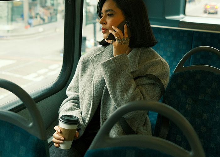 Woman on a bus, holding a coffee, talking on the phone, after being uninvited from a baby shower. Woman on a bus, holding a coffee, talking on the phone, after being uninvited from a baby shower.