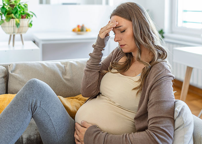 Pregnant woman looking stressed on couch, hand on forehead, related to baby shower food delivery conflict. Pregnant woman looking stressed on couch, hand on forehead, related to baby shower food delivery conflict.