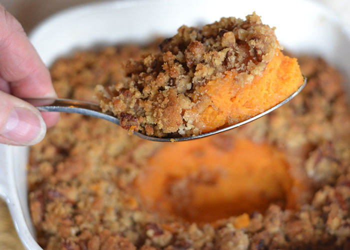 Thanksgiving dish being served with a spoon, featuring a sweet potato casserole topped with a pecan crumble. Thanksgiving dish being served with a spoon, featuring a sweet potato casserole topped with a pecan crumble.