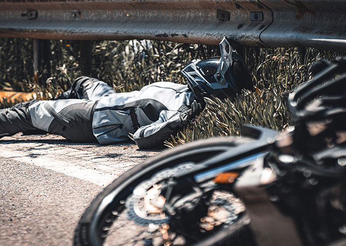 Motorcyclist lying on the roadside at night, wearing a helmet and suit, with a fallen bike nearby, depicting weird driving scenes. Motorcyclist lying on the roadside at night, wearing a helmet and suit, with a fallen bike nearby, depicting weird driving scenes.