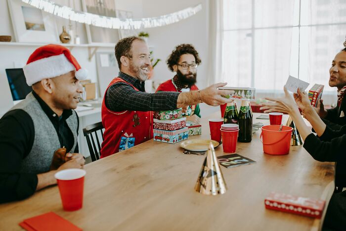 People exchanging Secret Santa gifts at a holiday gathering, with festive decorations and beverages on the table. People exchanging Secret Santa gifts at a holiday gathering, with festive decorations and beverages on the table.