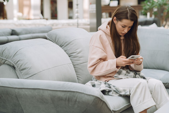 Single mother sitting on a gray sofa, focused on her smartphone, in a cozy living room setting. Single mother sitting on a gray sofa, focused on her smartphone, in a cozy living room setting.