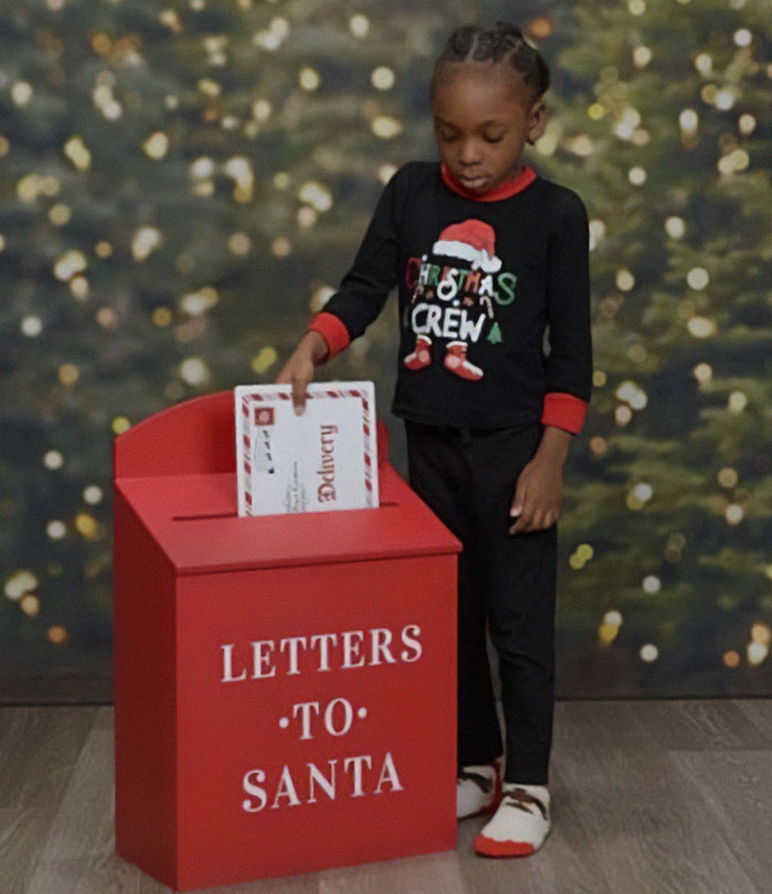 Child in Christmas pajamas at a Letters to Santa box, highlighting the son's unique attire in family photo. Child in Christmas pajamas at a Letters to Santa box, highlighting the son's unique attire in family photo.