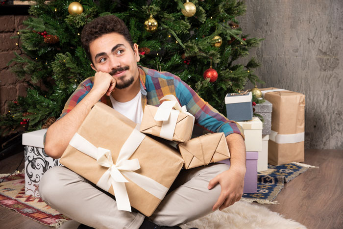 Person sitting with gifts by a Christmas tree, contemplating debt clearance for 1642 people using $5k intended for family gifts. Person sitting with gifts by a Christmas tree, contemplating debt clearance for 1642 people using $5k intended for family gifts.
