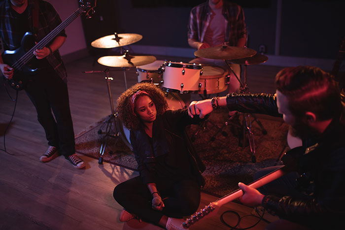 Woman sitting on a music stage with musicians, surrounded by drums and guitars, highlighting a peaceful life transition. Woman sitting on a music stage with musicians, surrounded by drums and guitars, highlighting a peaceful life transition.