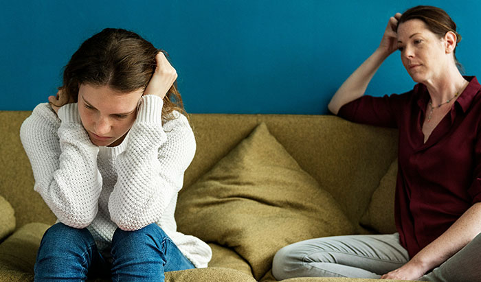 Mother and daughter having a serious discussion on a couch about daughter's money and family expectations. Mother and daughter having a serious discussion on a couch about daughter's money and family expectations.
