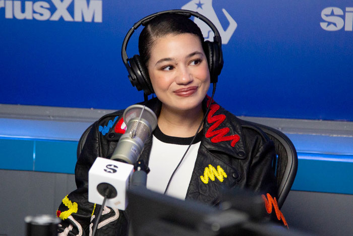 A cast member of "Tell Me Lies" in a radio interview, wearing headphones and a decorated black leather jacket.