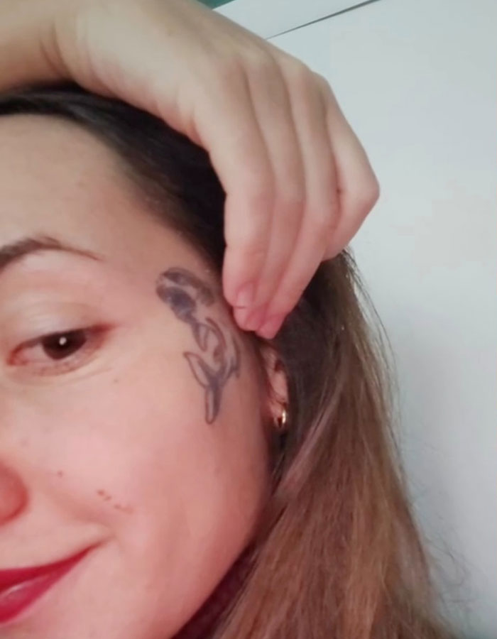 Woman with temporary tattoo on her cheek, smiling and holding her hair back. Woman with temporary tattoo on her cheek, smiling and holding her hair back.