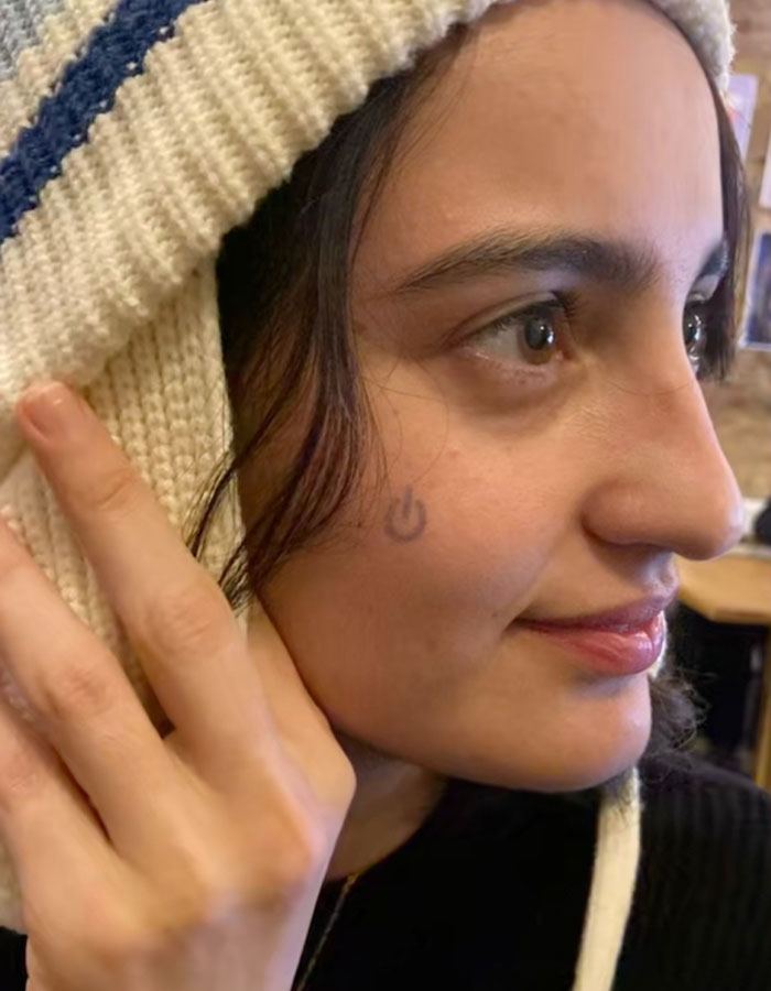 Woman with a temporary tattoo on her cheek, wearing a knit hat indoors. Woman with a temporary tattoo on her cheek, wearing a knit hat indoors.