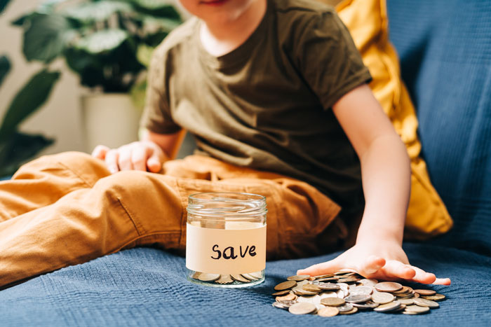 Child saving coins in a jar labeled "save" on a blue couch, prioritizing financial goals. Child saving coins in a jar labeled "save" on a blue couch, prioritizing financial goals.
