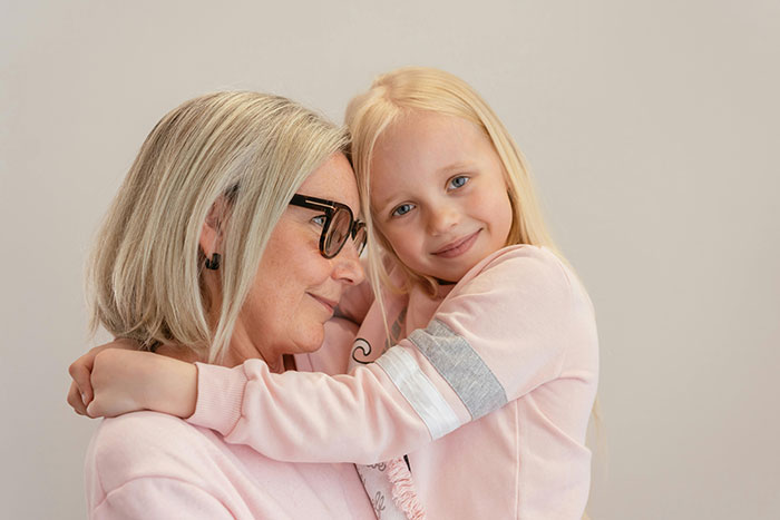 Grandmother hugging her granddaughter, both wearing pink sweaters, reflecting a close family bond despite recent tensions. Grandmother hugging her granddaughter, both wearing pink sweaters, reflecting a close family bond despite recent tensions.