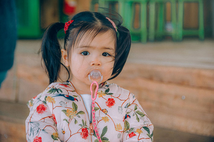 A young girl with pigtails and a pacifier, wearing a floral jacket, outdoors. A young girl with pigtails and a pacifier, wearing a floral jacket, outdoors.